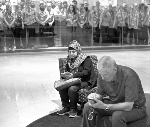 Two people looking at their smart phones in front of a window filled with shop assistants looking at shoppers