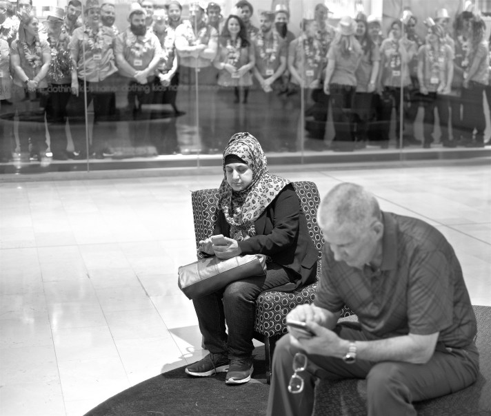 Two people looking at their smart phones in front of a window filled with shop assistants looking at shoppers