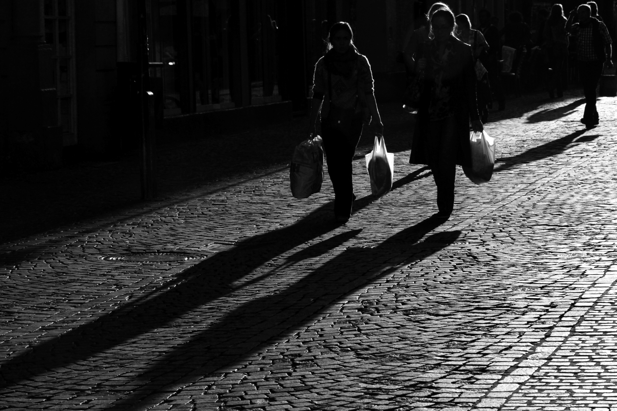 Backlit people walking down a cobblestone street