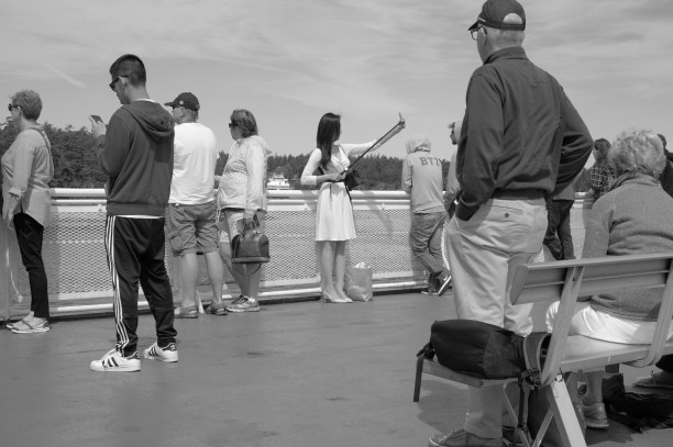 Photo of a lady on the deck of a ferry taking a selfie while surrounded by passengers