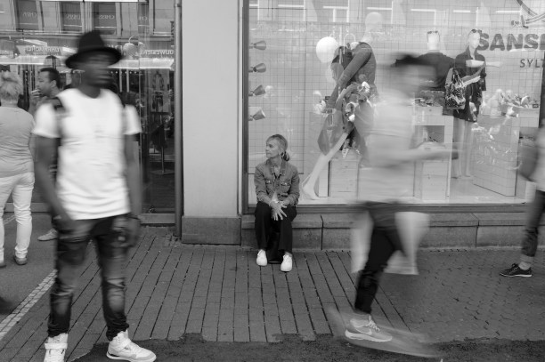 Woman sitting outside a fashion shop with people moving around her