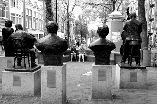 Bronze statue orchestra playing to a an audience of three women near a poster asking "What moves you?'